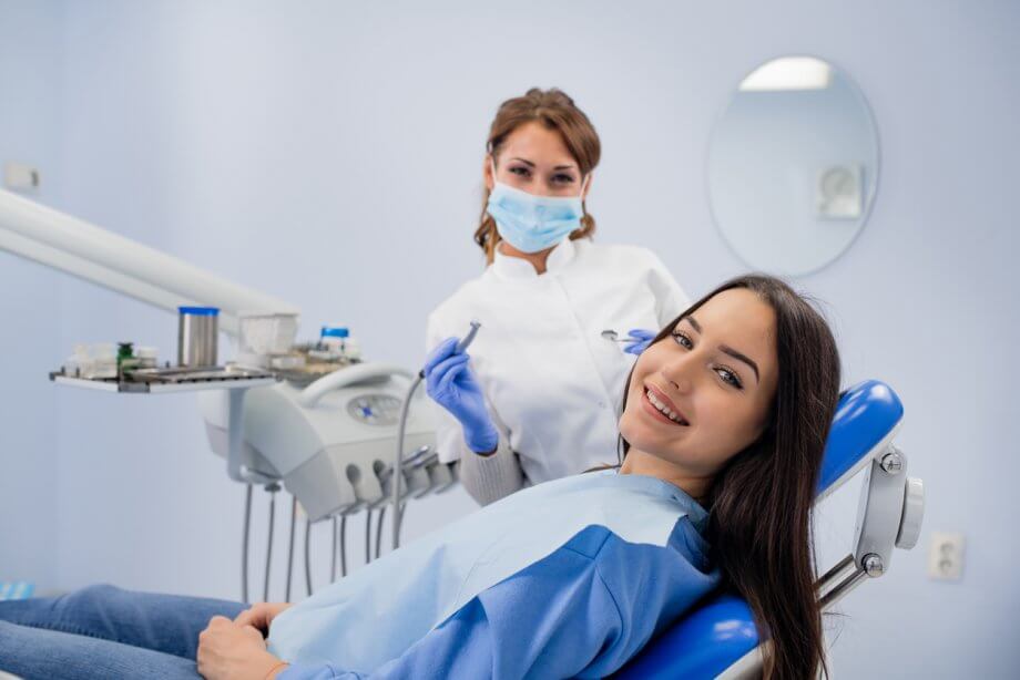 Happy young girl with long straight brown hair smiling in a dentist chair with a femail hygenist behind her.