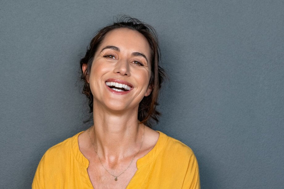 smiling woman in yellow shirt standing against grey background