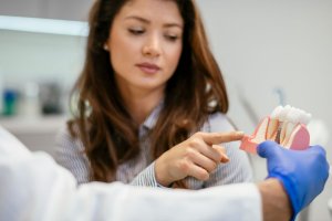 woman in dental chair pointing at dental implant model